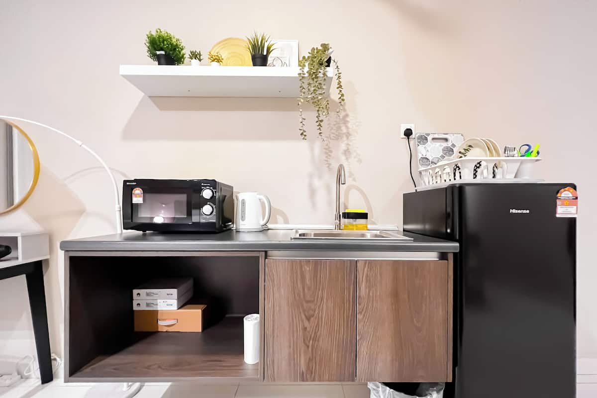 Una cocina moderna con microondas, cafetera y refrigerador. Hay una repisa con plantas y un pequeño armario debajo de la encimera.