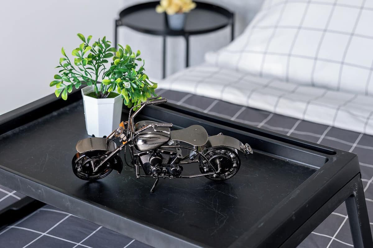 Un dormitorio ordenado con una cama, una mesita de noche con una planta y llaves, y una pequeña mesa con una maqueta de motocicleta.
