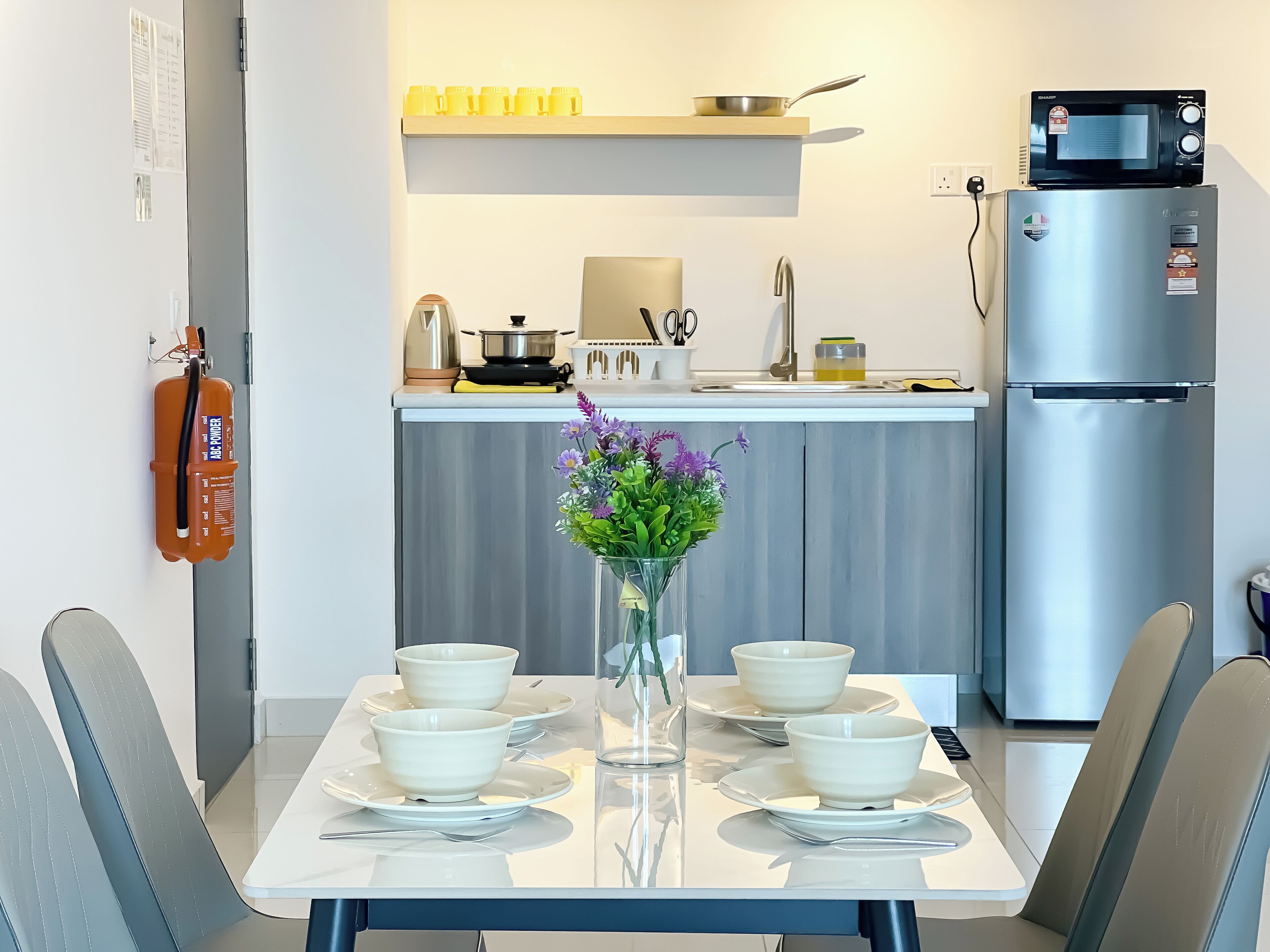 A modern kitchen with a dining table set for four, a microwave, a refrigerator, and a fire extinguisher on the wall.