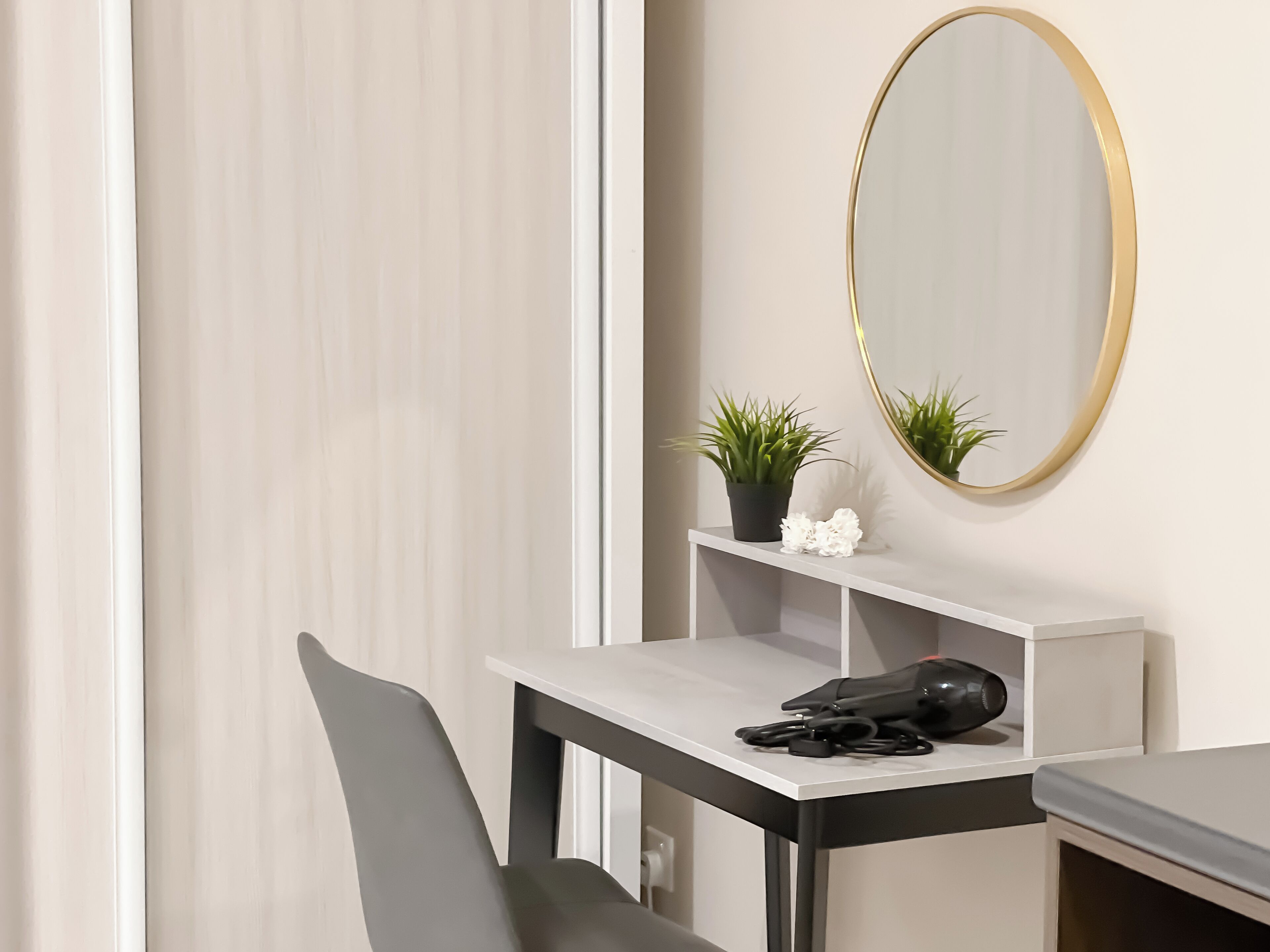 A modern room with a desk, chair, and a large mirror. There is a potted plant and a small white flower on the desk.