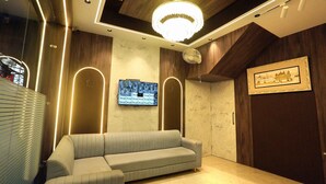 A modern living room with a sectional sofa, a large TV mounted on the wall, and a chandelier. - HOTEL GC GRAND INN (Amritsar)