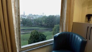 A room with a large window, a blue chair, a small table with water bottles, and a cabinet. - HOTEL GC GRAND INN (Amritsar)