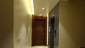A hallway with marble flooring, a wooden door at the end, and a staircase on the right. - HOTEL GC GRAND INN (Amritsar)