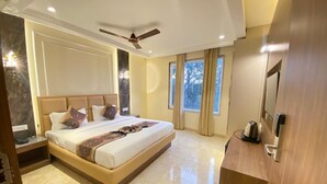 A spacious bedroom with a large bed, a ceiling fan, a wooden nightstand, and a wooden dresser. - HOTEL GC GRAND INN (Amritsar)