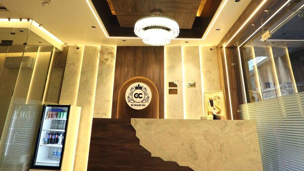 A hotel reception area with a marble counter, a spiral chandelier, and a logo on the wall. - HOTEL GC GRAND INN (Amritsar)