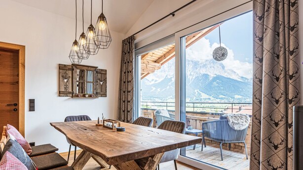 Un comedor con una amplia mesa de madera, sillas y vistas a las montañas a través de grandes ventanales.