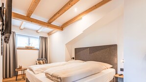 Un dormitorio con una cama grande, vigas de madera, una mesita y una ventana con cortinas.