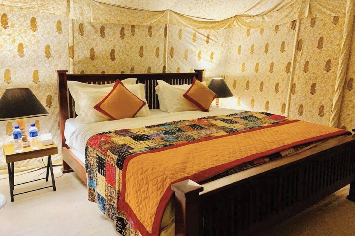 A hotel room with a large bed, two bedside lamps, a nightstand with water bottles, and patterned wallpaper.