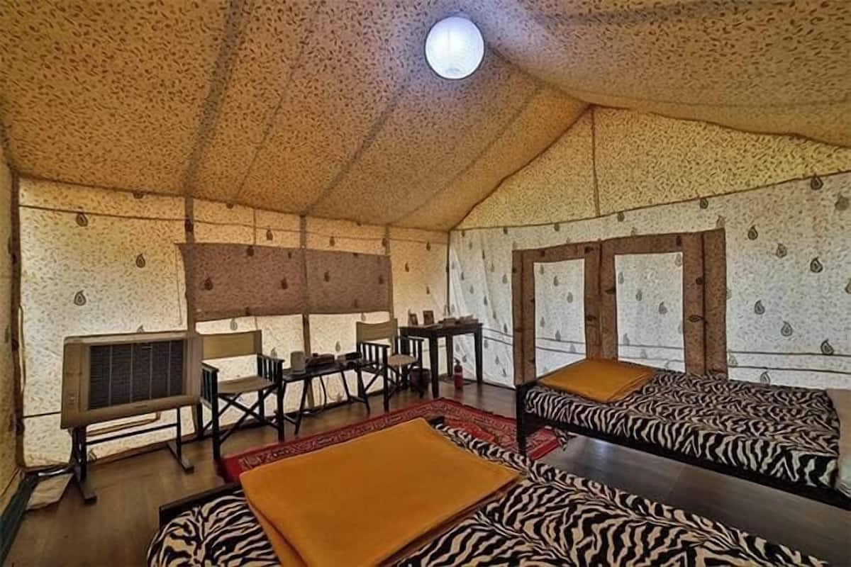 A tent-style room with zebra-patterned bedding, a wooden table, chairs, and a small rug.