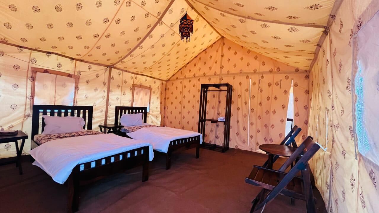 A tented room with two beds, a small table, and a chair.