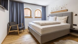 Une chambre moderne avec un grand lit, une chaise, deux fenêtres avec des rideaux et un luminaire au plafond.