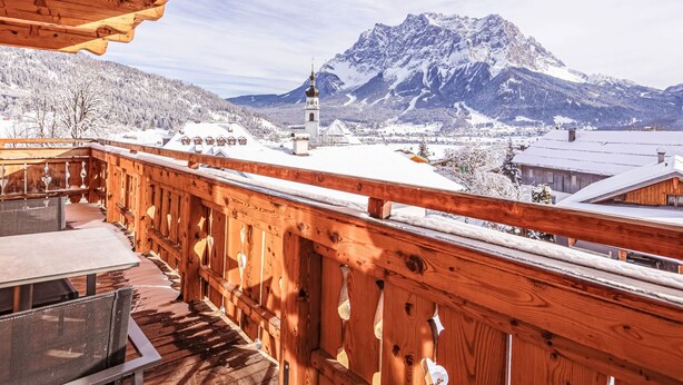 Un balcón de madera con vista a una montaña nevada y la aguja de una iglesia.