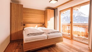 Una cama de madera en una habitación con un ventanal y vistas a montañas.
