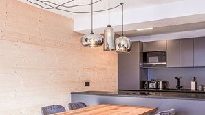 Une cuisine moderne avec une table à manger en bois, des chaises grises et des luminaires suspendus.