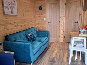 A room with a blue sofa, a small table with chairs, wooden walls, and a door.