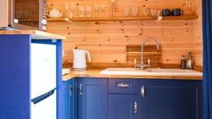 Une petite cuisine équipée d’un four à micro-ondes, d’un évier et d’étagères en bois où sont rangés de la vaisselle et des tasses.