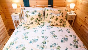 Une chambre dans un chalet en bois, avec un lit, deux tables de chevet et une lampe de chevet de chaque côté.