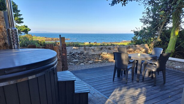 Un bain à remous, une terrasse en bois, une table et des chaises d’extérieur, et une vue sur la mer.