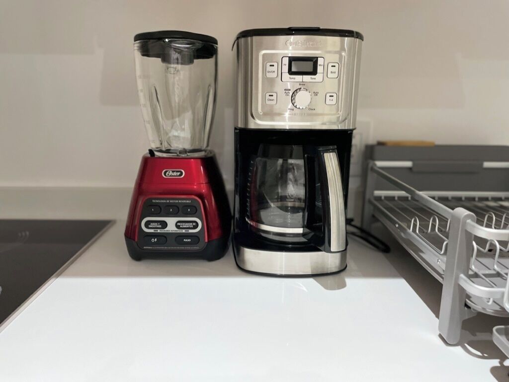 A red Oster blender and a silver Oster coffee maker on a white countertop.