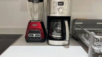 A red Oster blender and a silver Oster coffee maker on a white countertop.