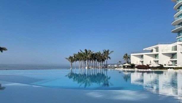 A clear blue pool with palm trees in the center, surrounded by a white building with balconies.