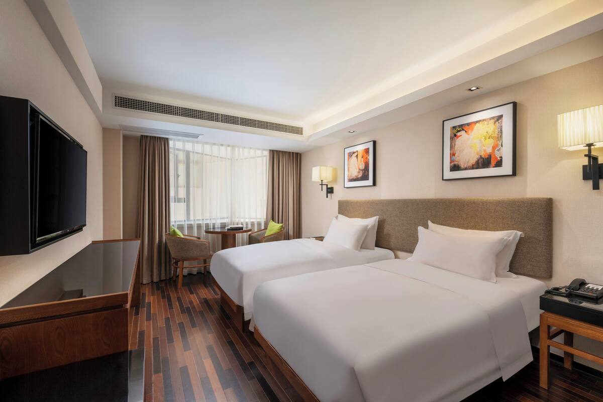 A hotel room with two beds, a TV, a desk with a phone, a chair, and a window with curtains.