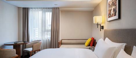 A hotel room with a large bed, a desk with a chair, a sofa, a lamp, and a picture on the wall.