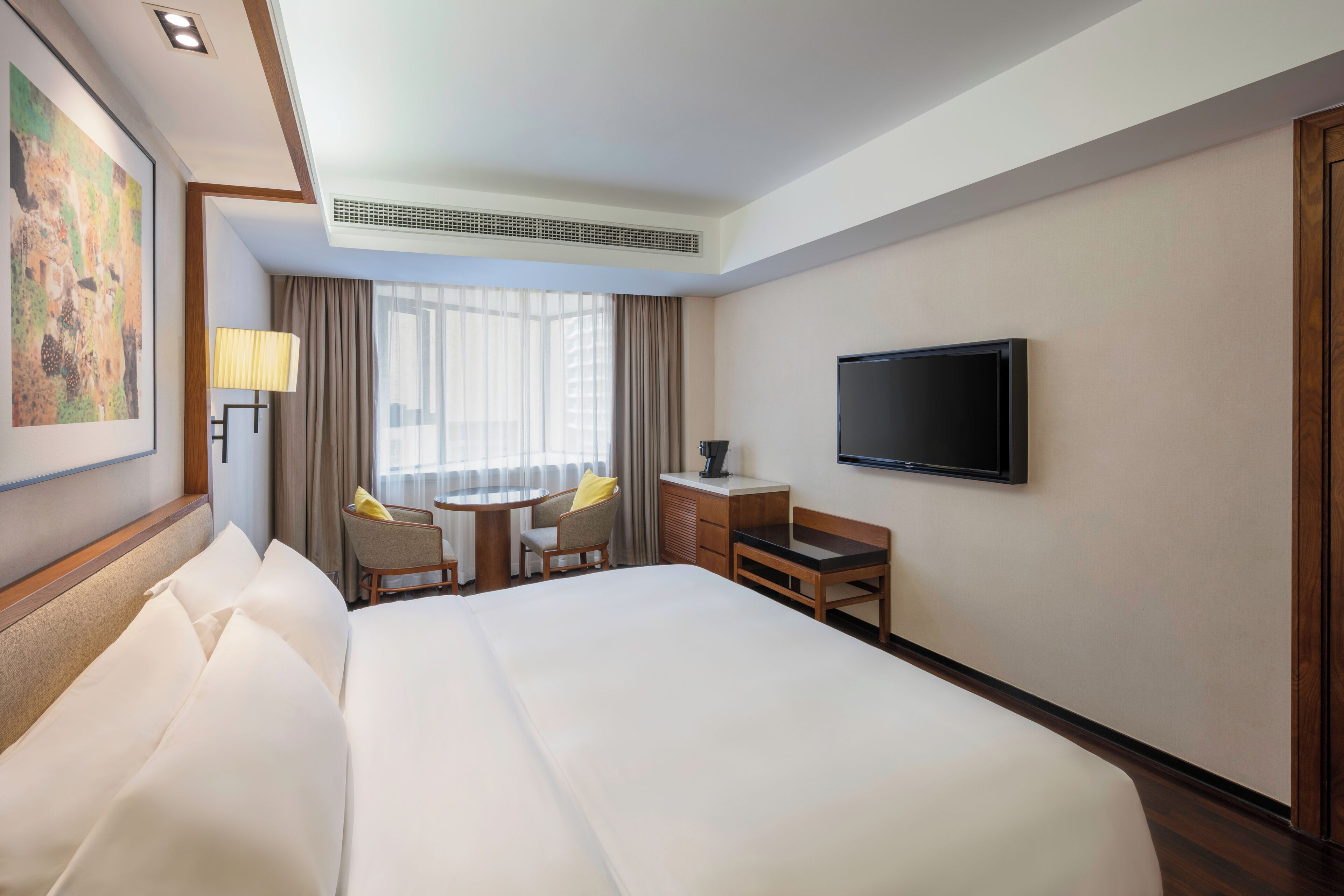 A hotel room with a large bed, a desk with two chairs, a television, and a window with curtains.