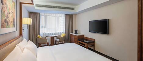A hotel room with a large bed, a desk with two chairs, a television, and a window with curtains.