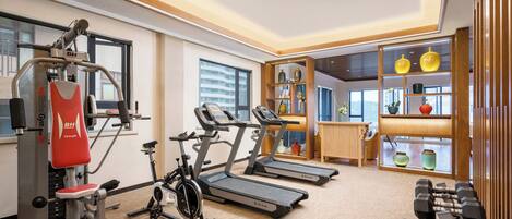 A gym with exercise equipment, including treadmills and a stationary bike, and a weight bench with dumbbells.