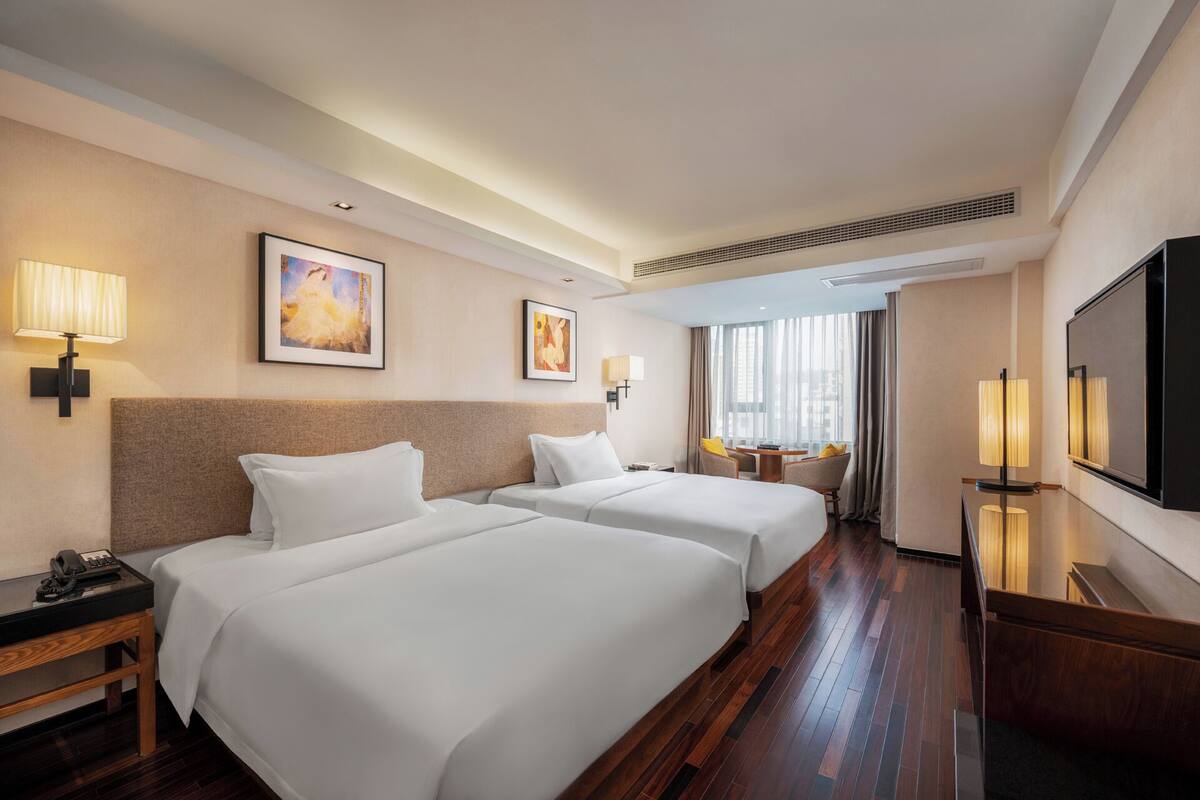 A hotel room with two beds, a desk with a phone, a TV, and artwork on the walls.