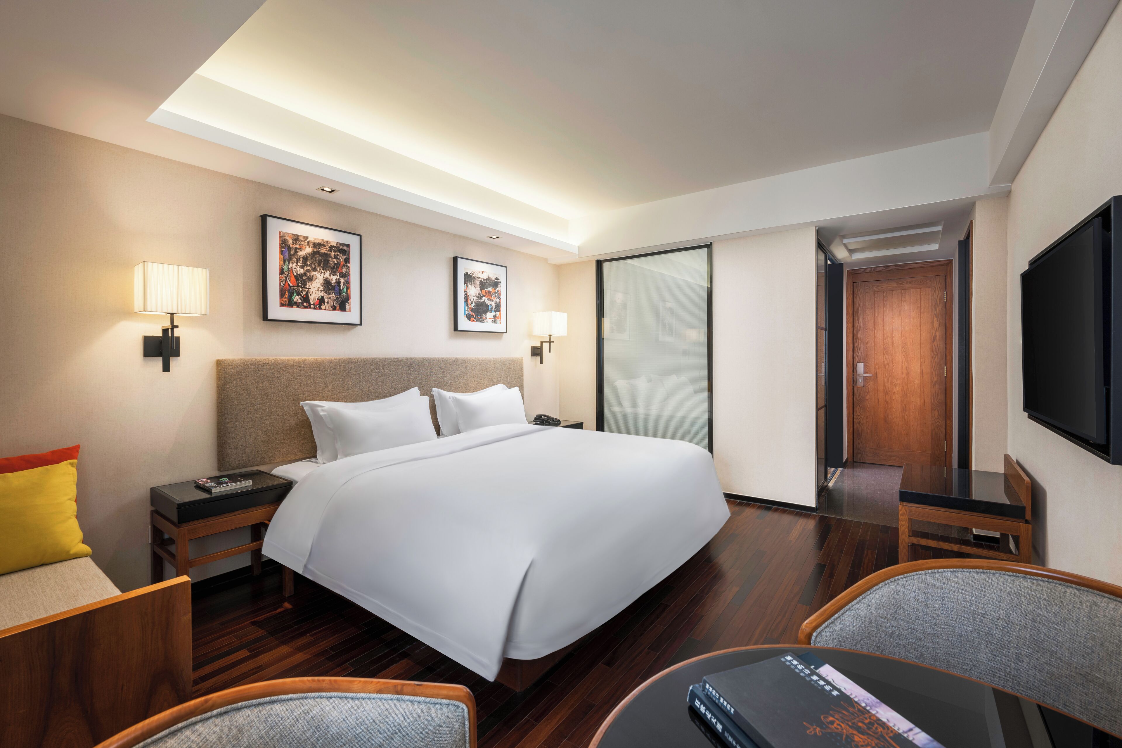Een hotelkamer met een groot bed, nachtkastjes, een bureau met stoel, een televisie en kunstwerken aan de muren.