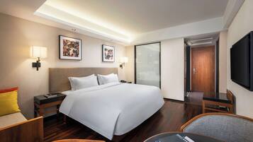 Habitación de hotel con una cama grande, mesitas de noche, un escritorio con una silla, televisión y obras de arte en las paredes.