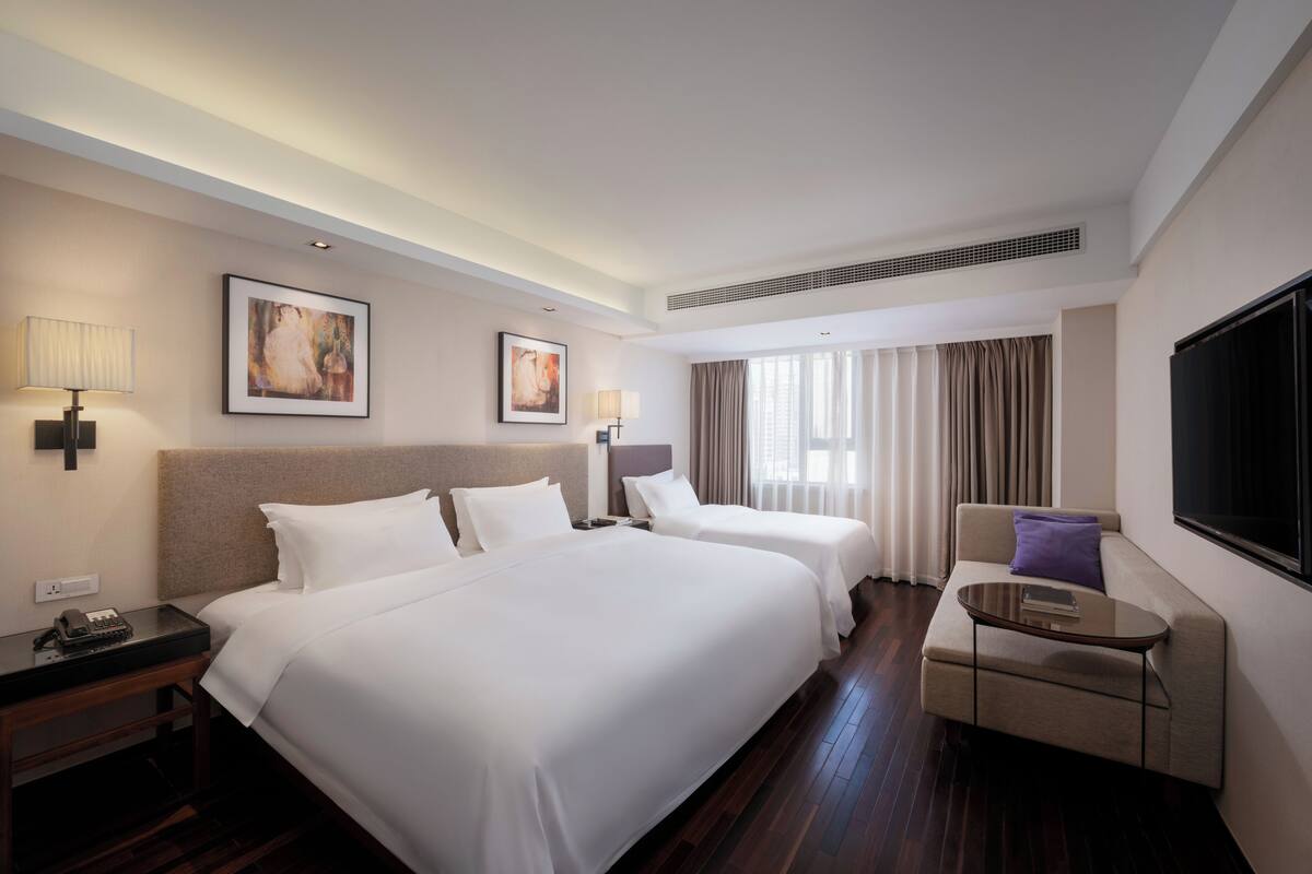 A hotel room with two beds, a sofa, a TV, and artwork on the walls.