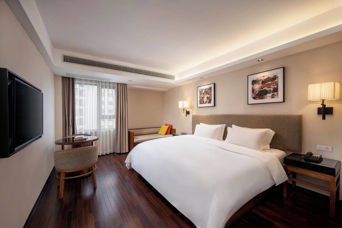 A hotel room with a large bed, a TV, a seating area with a table and chairs, and artwork on the walls.