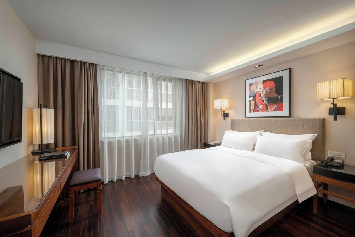 A hotel room with a large bed, a desk with a chair, a TV, and a painting on the wall.