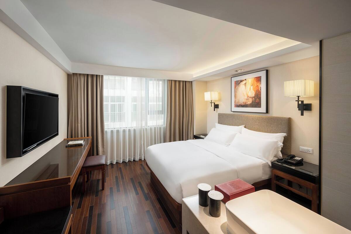 A hotel room with a large bed, a desk, a television, and a window with curtains.