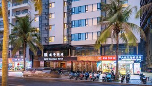Un hotel de varios pisos con fachada moderna, balcones y zona comercial en la planta baja.
