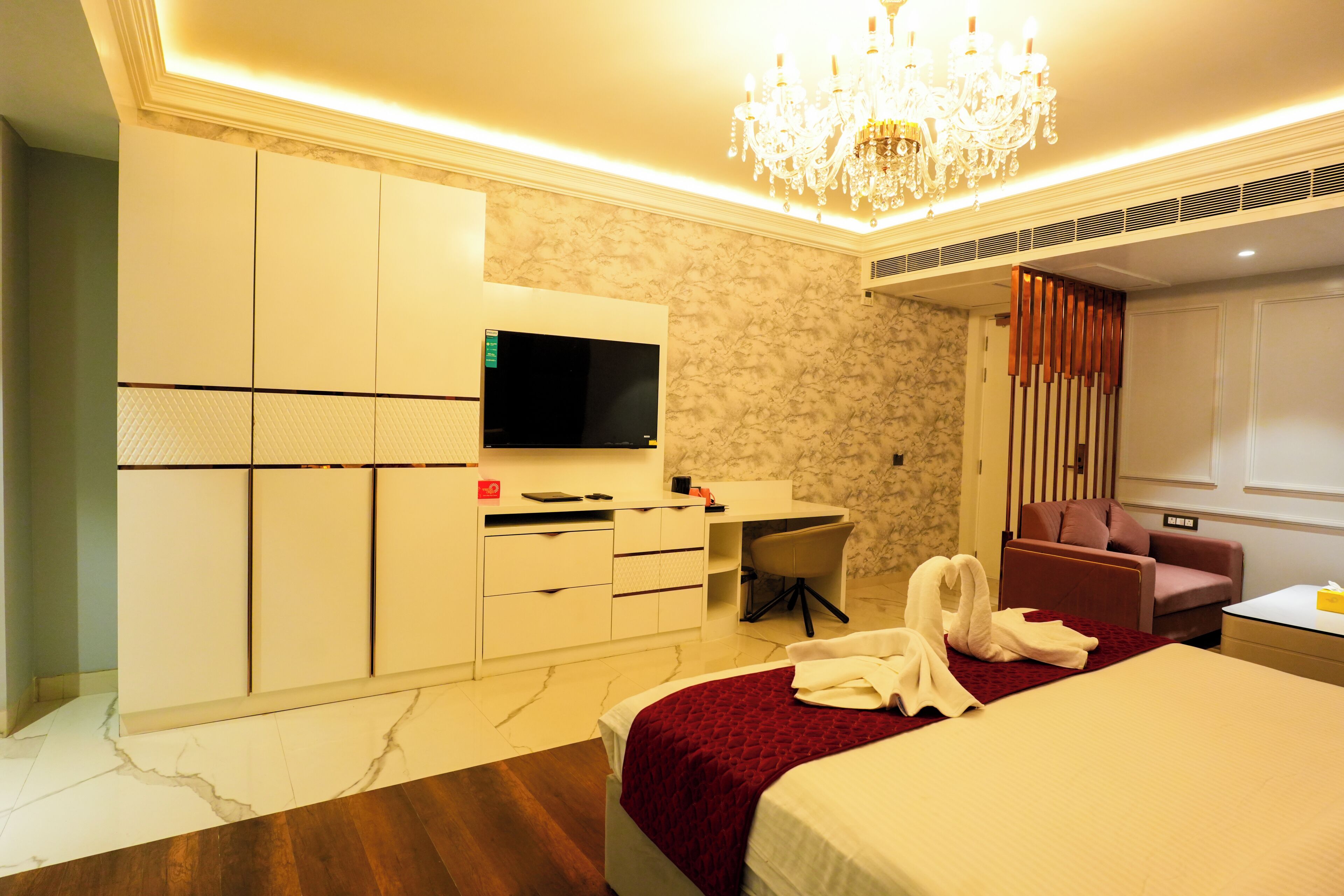 Une chambre d’hôtel comprenant un lit, un bureau, une télévision, un lustre et un coin salon.