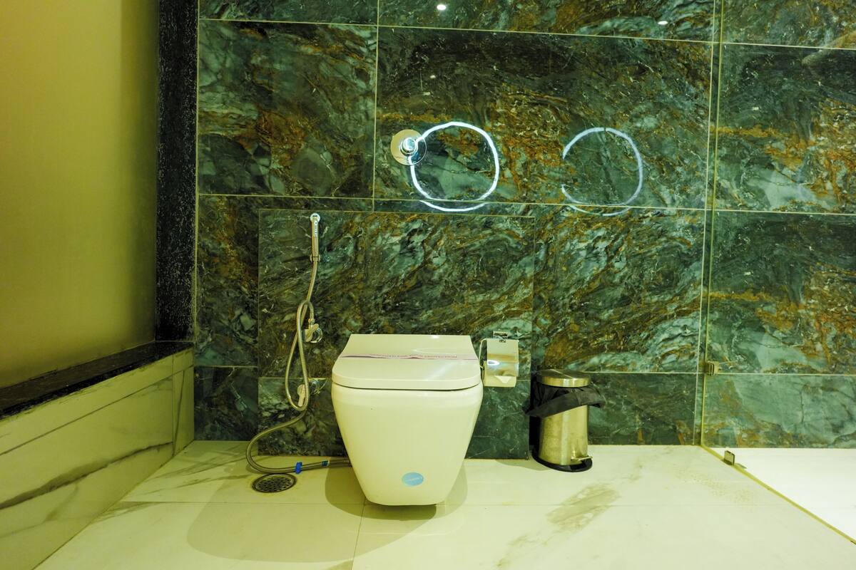 Une salle de bain avec un mur en marbre, des toilettes, une poubelle et un tuyau de douche.