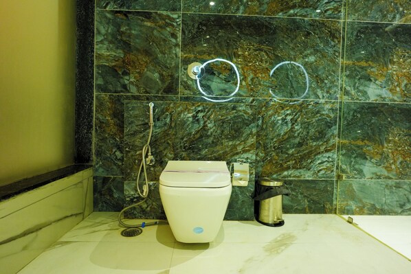 A bathroom with a marble wall, a toilet, a trash bin, and a shower hose.