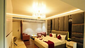 Een moderne hotelkamer met een groot bed, een zithoek met een bank en fauteuils, een bijzettafeltje en een kroonluchter.