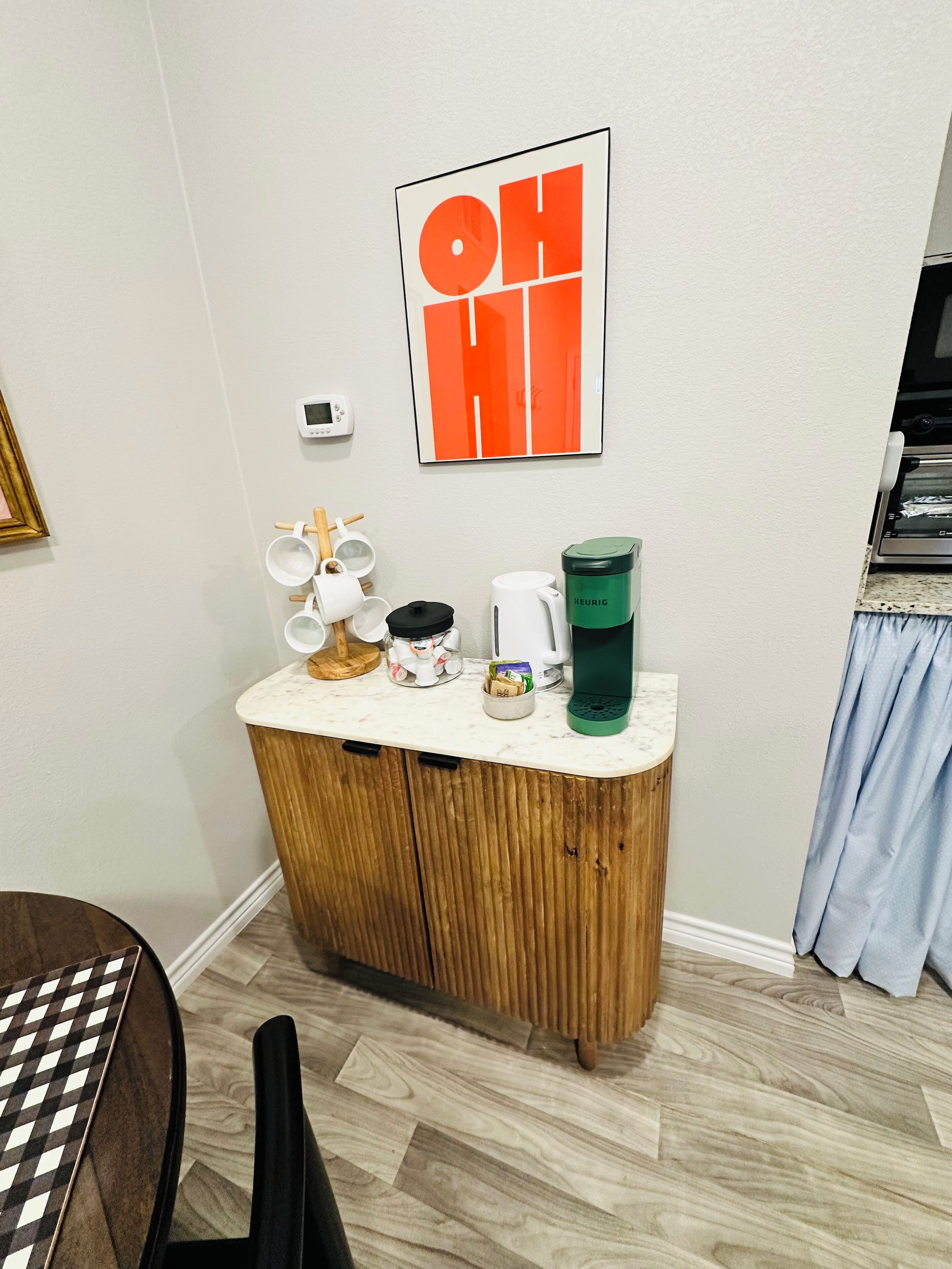 Una kitchenette con cafetera, hervidor y soporte para cápsulas Keurig sobre una encimera de mármol.