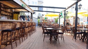 Un cafè a l'aire lliure amb taules i cadires de fusta, una zona de bar i paraigües grocs que ofereixen ombra.