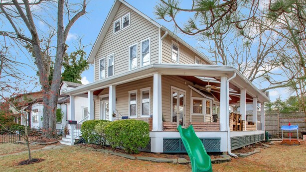 Une maison à deux étages avec un porche, un toboggan vert et une cour arrière clôturée.