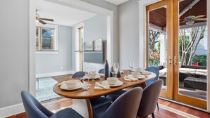 Un coin repas avec une table dressée pour quatre personnes, un ventilateur de plafond et une porte-fenêtre coulissante donnant sur une terrasse extérieure.