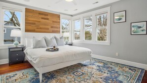 Une chambre à coucher avec un lit, un panneau mural en bois, de grandes fenêtres, un ventilateur de plafond et un tapis à motifs.