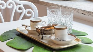 A table with a tray of food, a cup, and a glass. There are potted plants on the windowsill.