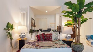 A bedroom with a bed, two bedside tables, a nightstand, a potted plant, a lamp, and a mirror.