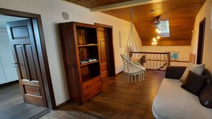 A cozy room with a wooden floor, a sofa, a wooden cabinet, a hammock, and a staircase leading to a loft area. - Vacation home Rötzer - Forsthausschmankerl (Bruck in der Oberpfalz)